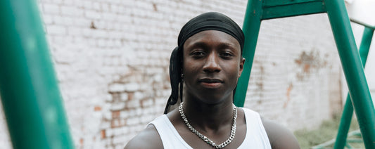 Black man wearing a black durag stands at a park.